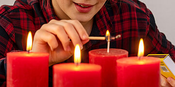 Foto_ Ein Kind im roten Schlafanzug zündet die vierte Adventskerze mit einem Streichholz an.