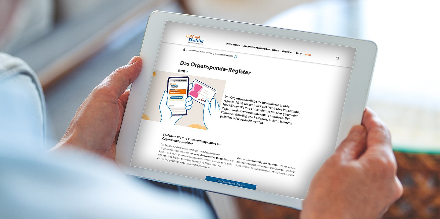 Foto: Ein sitzender Mensch hält ein Tablet, darauf ist das digitale Organspenderegister zu sehen.