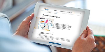 Foto: Ein sitzender Mensch hält ein Tablet, darauf ist das digitale Organspenderegister zu sehen.