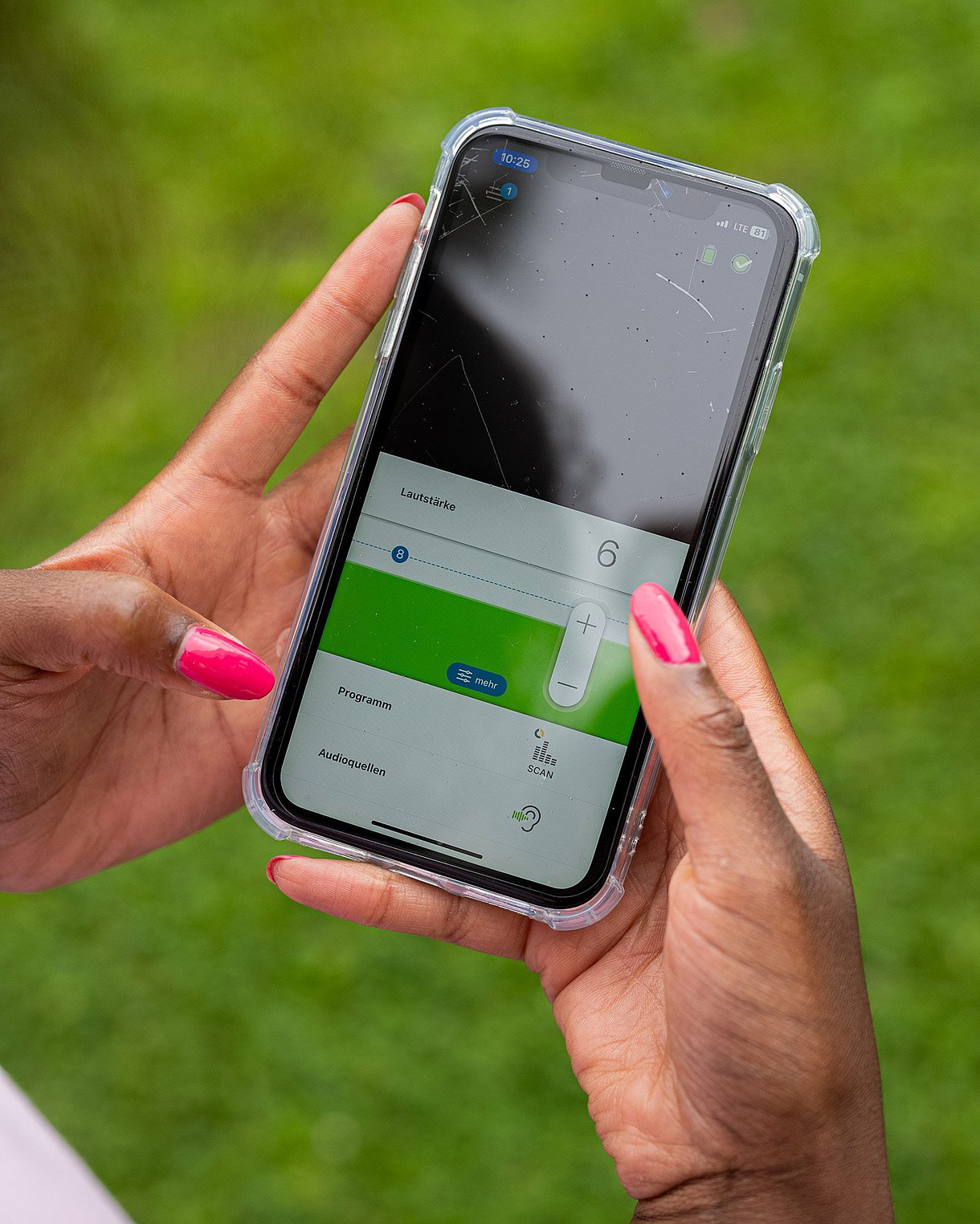 Foto eines Handys, das von zwei weiblichen Händen gehalten wird. Auf dem Handy wird eine App zur Sprachsteuerung eines Cochlea-Implantats angezeigt