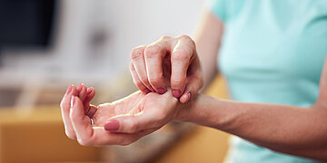 Foto: Eine Frau, von der man nur Oberk&ouml;rper, Arm und Hand sieht, kratzt sich am Handgelenk.