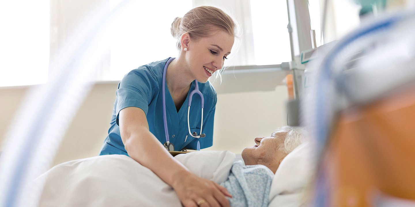 Das Foto zeigt eine Pflegerin, die eine alte Frau im Kranken zimmer bettet.