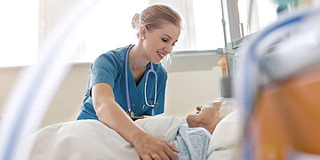 Hochbetagte Senioren Krankenhaus 1 Das Foto zeigt eine Pflegerin, die eine alte Frau im Kranken zimmer bettet.