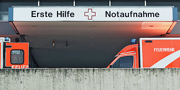 Der Eingang zur Notaufnahme: Zwei Rettungsfahrzeuge stehen vor dem Einfang. &Uuml;ber dem Eingang steht auf dem Schild "Erste Hilfe" und "Notaufnahme".