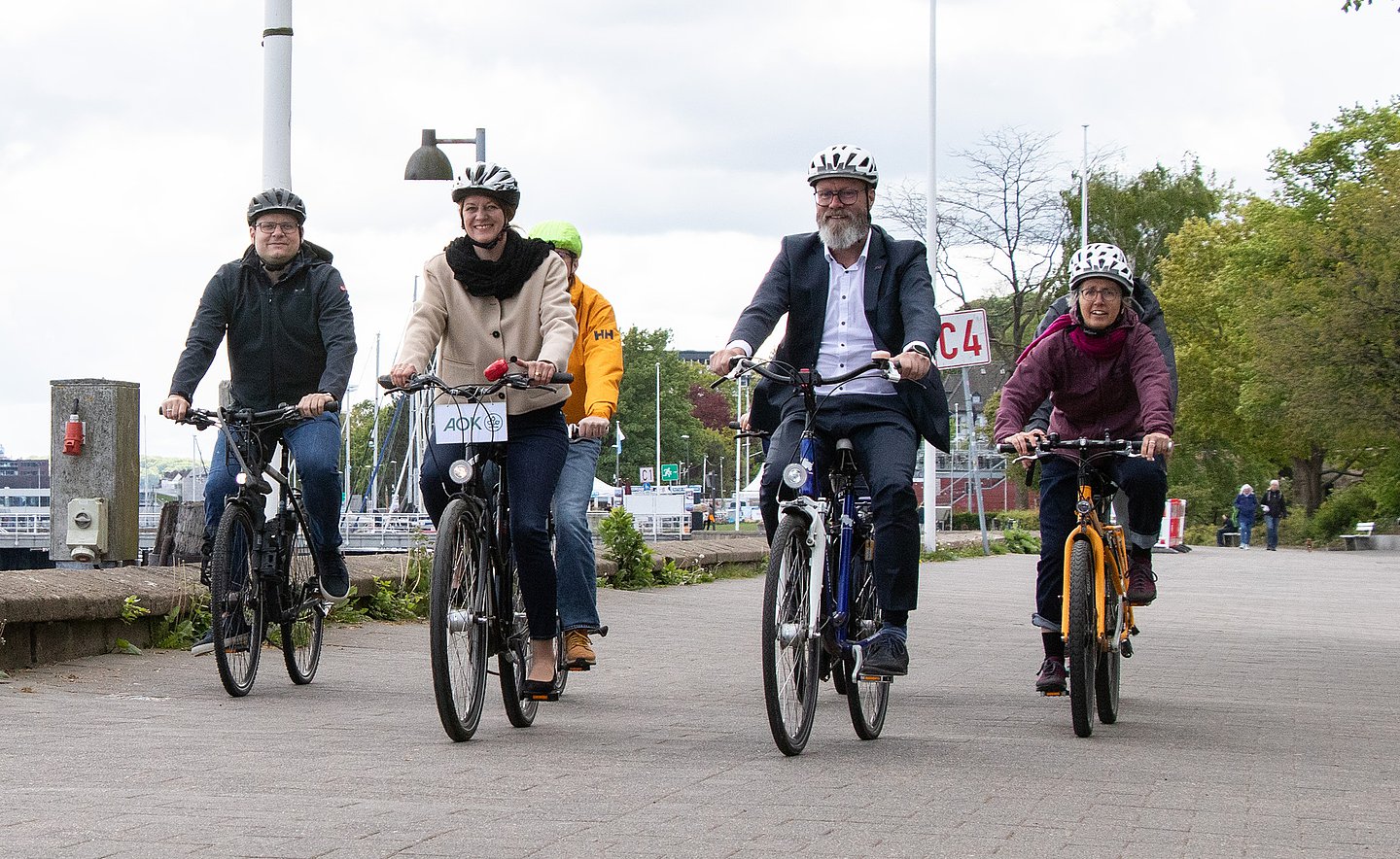 An der Kiellinie radeln Landes-Verkehrsminister Claus Ruhe Madsen (rechts) und AOK-Landesdirektorin Iris Kröner (links) mit Beschäftigten des Landes-Verkehrsministeriums.