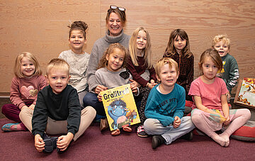 Das Foto zeigt die AOK-Landesdirektorin Iris Kr&ouml;ner beim Vorlesen umringt von Kindergartenkinder.