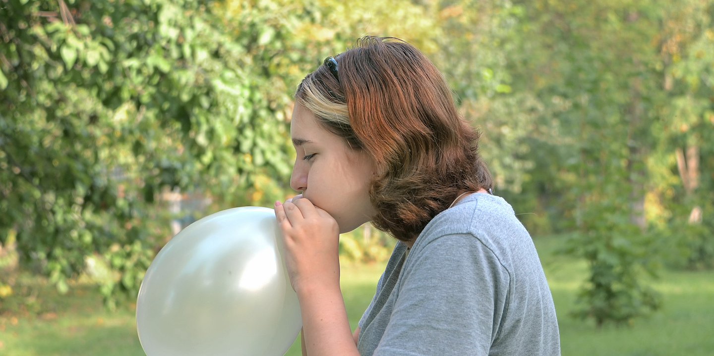Ds Foto zeigt ein Mädchen, das in einen Ballon bläst.