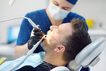 Ein Patient in einem Zahnarztstuhl wird von einem Zahnarzt mit einem Bohrer behandelt.