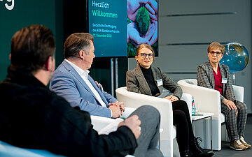 Der Moderator Michael Bernatek und die Referenten Holger Westermann, Dorothea Baltruks und Veronika B&auml;cker sitzen auf dem Podium. 