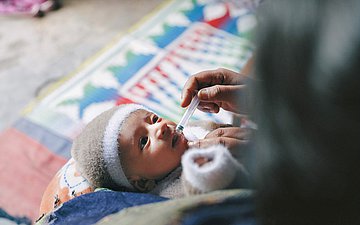 Eine Frau gibt einem kleinen Baby die Impftropfen.