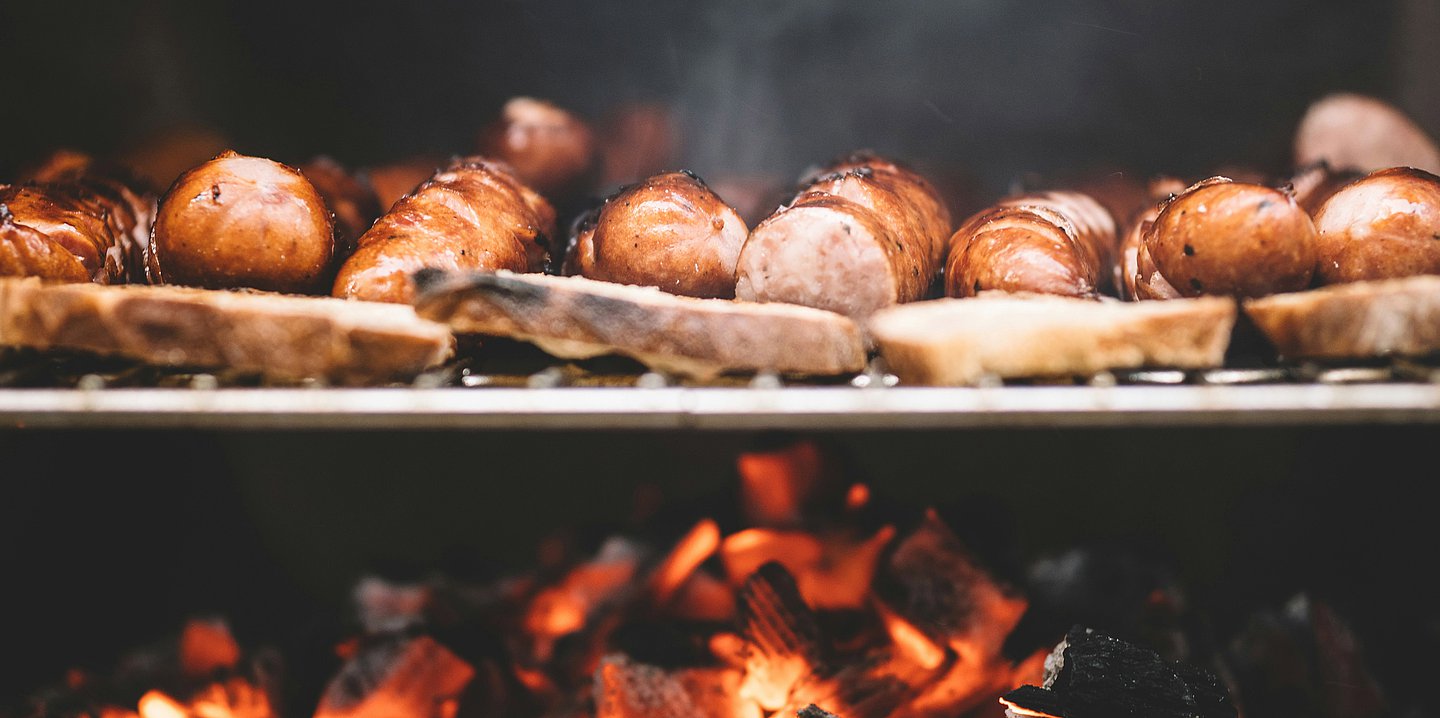 Foto: Würstchen und Weißbrot liegen auf einem Holzkohlegrill.