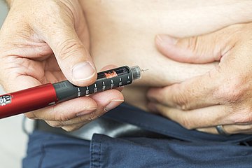 Eine ältere Person injiziert sich Insulin mit einem Pen in den Bauch.