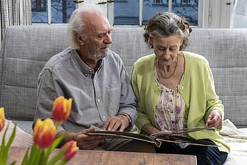 Ein &auml;lterer Mann und eine &auml;ltere Frau sitzen auf einem Sofa und schauen sich ein Fotoalbum an.