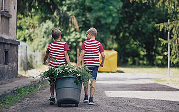 Zwei Kinder ziehen eine Tonne mit Gr&uuml;nabf&auml;llen.