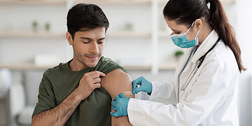 Nach einer Impfung klebt die &Auml;rztin einem Patienten ein Pflaster auf den Arm.