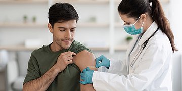 Hepatitis Impfung Nach einer Impfung klebt die Ärztin einem Patienten ein Pflaster auf den Arm.