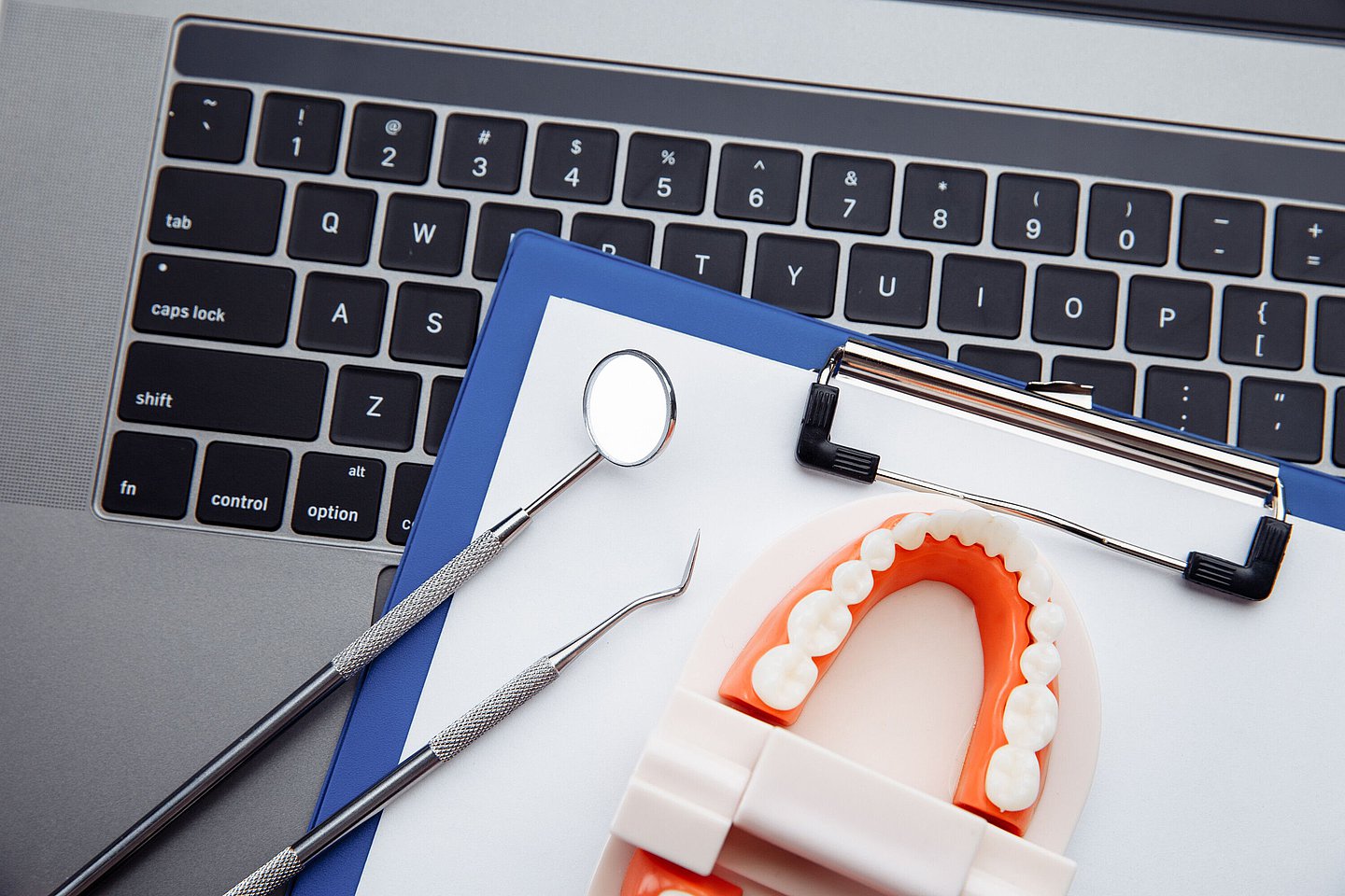 Zahnarztbesteck liegt mit einer Klemmmappe auf einer Tastatur.
