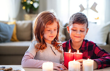Das Foto zeigt ein M&auml;dchen und einen Jungen, die sich brennende Kerzen anschauen.