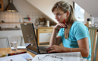 Eine Frau arbeitet zu Hause. Sie sitzt am K&uuml;chentisch mit ihrem Computer.