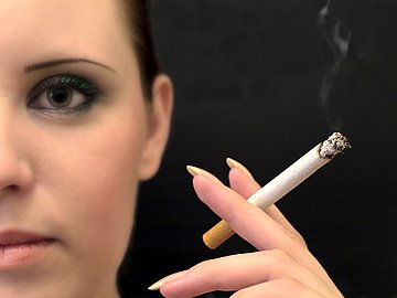 Rauchen und Krankenhauseinweisungen in Schleswig-Holstein Sichtbar ist die Gesichtshälfte einer Frau, die vor schwarzem Hintergrund neutral zum Betrachter blickt. In der linken Hand, zwischen Zeige- und Mittelfinger, hält sie auf Gesichtshöhe eine brennende Zigarette.