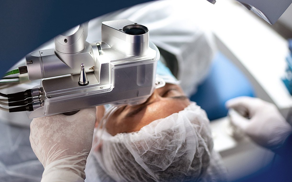 Kopf eines Patienten mit OP-Haube, der am Auge operiert wird, OP-Apparatur oberhalb der Augenpartie
