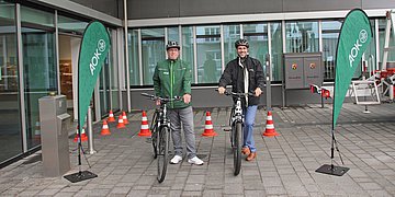 Auftakt mit dem Rad zur Arbeit in Rheinland-Pfalz Foto zeigt zwei Männer mit Helm und Fahrrad vor einem Verwaltungsgebäude