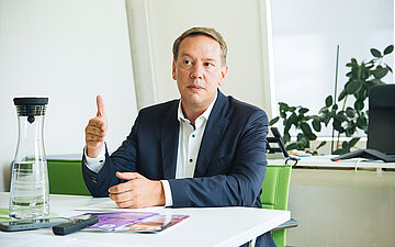 Herr Hildenbrand sitzt ein einem Tisch und macht eine Handgeste.