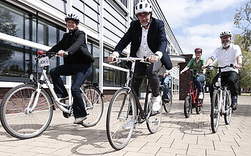F&uuml;nf Radfahrende vorm Danfoss-Geb&auml;ude in Neum&uuml;nster. 