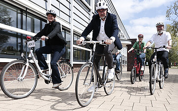 F&uuml;nf Radfahrende vorm Danfoss-Geb&auml;ude in Neum&uuml;nster. 