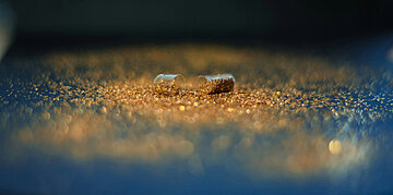 Ge&ouml;ffnete Medikamentenkapsel, deren zwei H&auml;lften auf einer goldfarben schimmernden Oberfl&auml;che liegen.