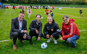 Kita-Cup 2025 Vier Personen positionieren sich mit einem Ball auf dem Rasen eines Fußballstadions.