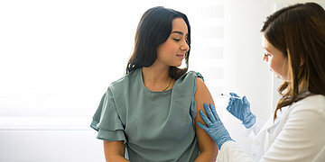 Eine junge Frau wird von einer &Auml;rztin geimpft und bekommt dazu eine Spritze in den Oberarm.