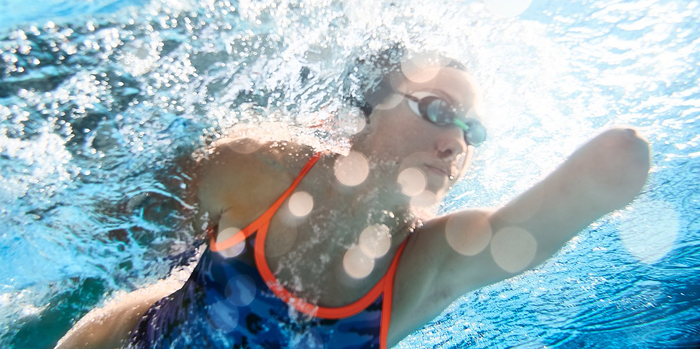 Foto: Eine Frau ohne Unterarme schwimmt in Badekleidung durch Wasser.