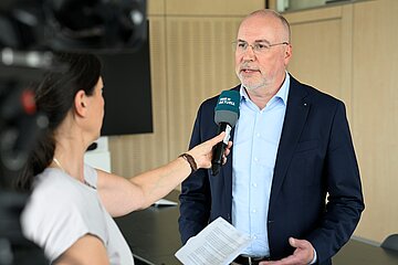 Eine Journalistin h&auml;lt Johannes Bauerfeind in einer Interview-Situation ein Mikrofon hin.