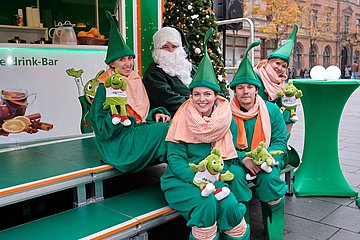 Am AOK-Stand erwarten der grüne Weihnachtsmann und seine Wichtel die Besucher auf insgesamt acht Weihnachtsmärkten in Sachsen-Anhalt. Foto der AOK-Wichtel am Spendenstand der AOK Sachsen-Anhalt