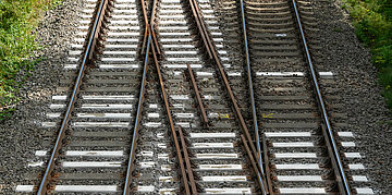 Foto: Blick von oben auf mehrere Bahngleise mit einer Weiche. Die Schienen verzweigen sich und f&uuml;hren in unterschiedliche Richtungen.