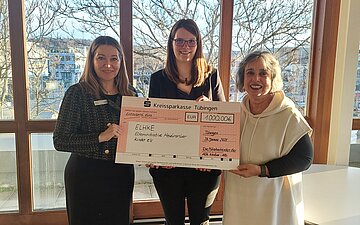 Drei Frauen halten gemeinsam ein gro&szlig;es Scheckformular: Marion Rostam, Domenika Brodbeck und Mita Ettischer.