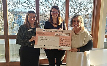 Scheckübergabe Drei Frauen halten gemeinsam ein großes Scheckformular: Marion Rostam, Domenika Brodbeck und Mita Ettischer.