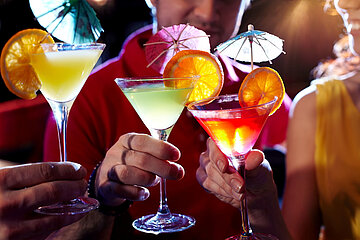 Zwei Frauen und ein Mann in Nahaufnahme sto&szlig;en mit bunten Cocktails an.