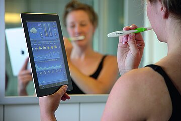 Eine Jugendliche schaut selbst beim Z&auml;hneputzen auf ihr Tablet.