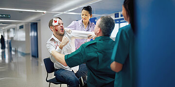 Foto: Ein Patient mit blutigem Gesicht und Verb&auml;nden geht auf Klinikpersonal los.