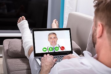 Videosprechstunden in Westfalen-Lippe Mann mit Beinverletzung kommuniziert per Tablet mit seinem Arzt.