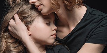 Eine Frau umarmt ein traurig wirkendes Mädchen
