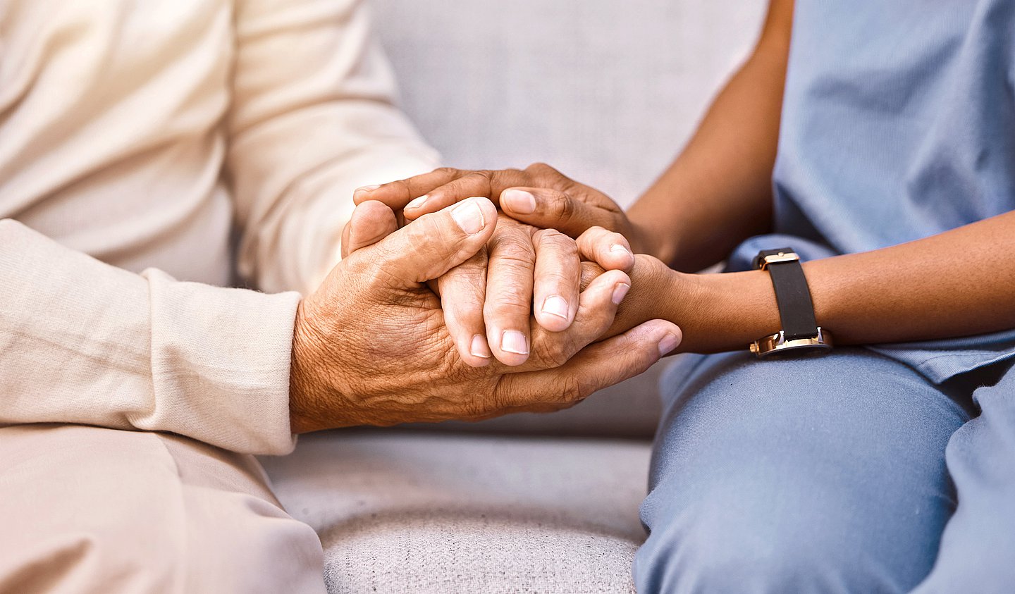 Foto: Eine Pflegefachkraft und eine pflegebedürftige Person halten Hände