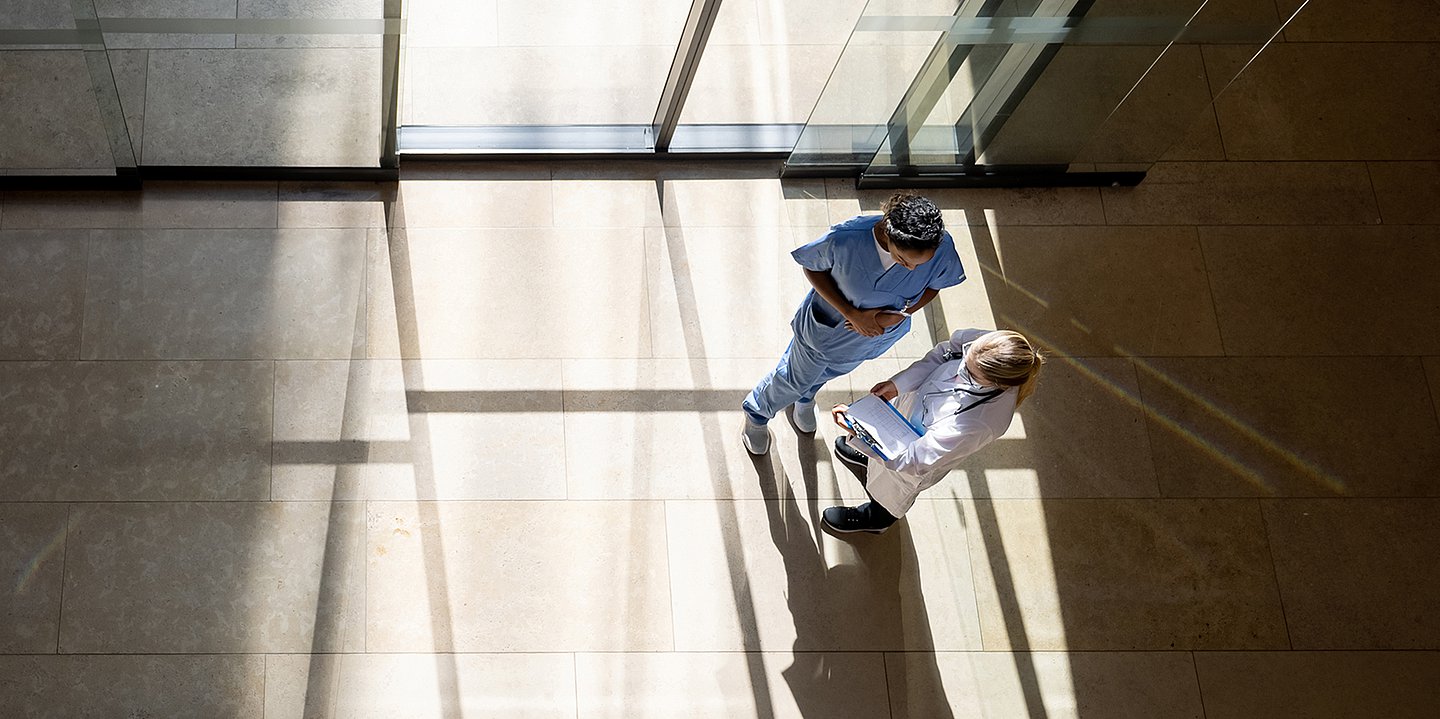 Foto: Blick von oben auf eine Pflegerin und eine Medizinerin in einem Eingangsbereich