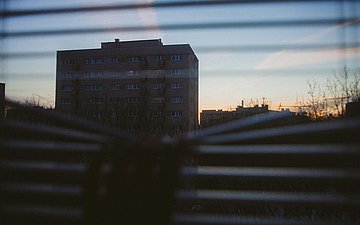 Foto: Blick durch ein Rollo auf ein großes Gebäude bei Sonnenuntergang.