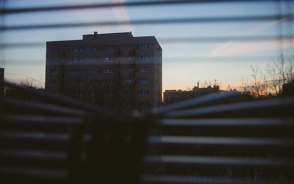 Foto: Blick durch ein Rollo auf ein großes Gebäude bei Sonnenuntergang.