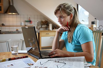 Eine Frau arbeitet zu Hause. Sie sitzt am Küchentisch mit ihrem Computer.