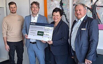 &Uuml;bergabe eines gro&szlig;en Spendenschecks in Rastatt: Vier Personen schauen in die Kamera, in der Mitte halten zwei von ihnen einen gro&szlig;en Spendenscheck.