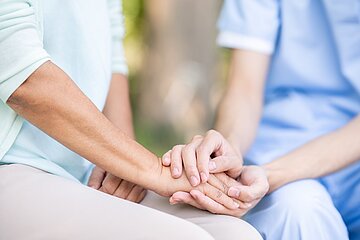 Die H&auml;nde einer Pflegerin halten eine Hand einer anderen Person.